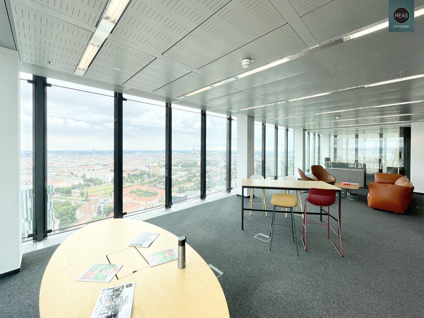 Moderner Bürobereich mit großem ovalen Tisch und einer gemütlichen Sitzecke, bietet Stadtpanorama.