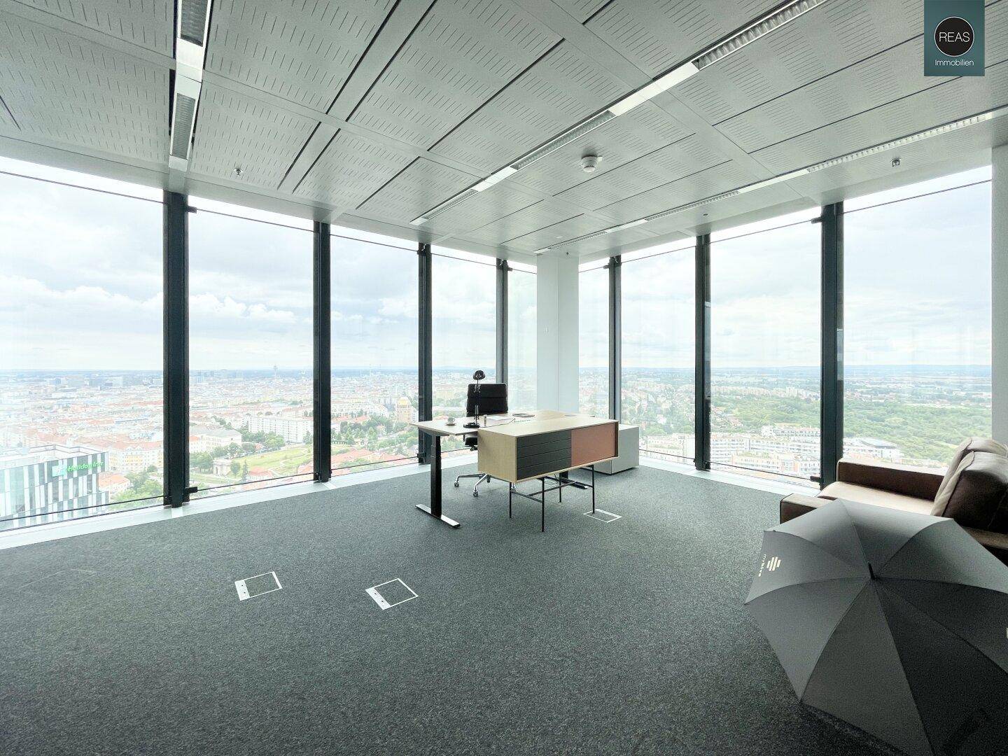 Einzelbüro mit Schreibtisch und Ledersofa, großen Fenstern und weitem Blick über die Stadtlandschaft.