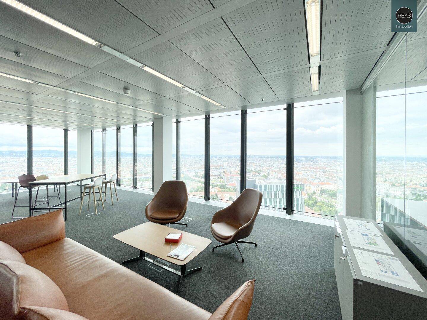 Moderner Büroraum mit Ledersofa, Lounge-Sesseln und raumhohen Fenstern mit weitem Stadtblick.