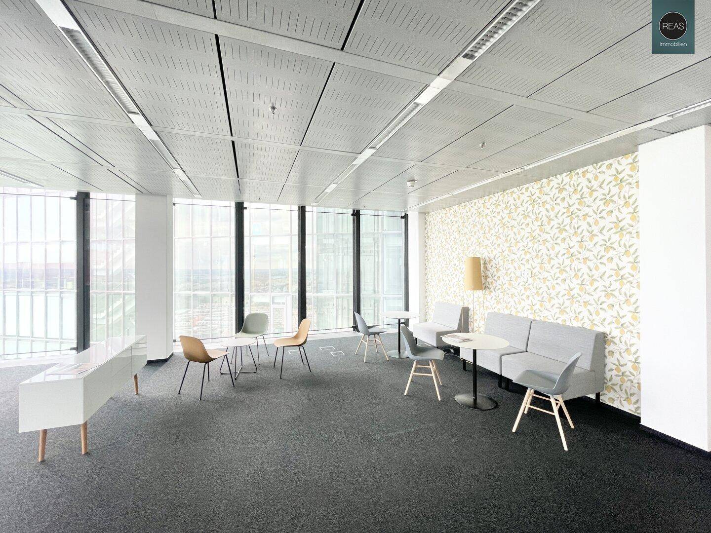 Moderner Bürobereich mit Lounge-Möbeln und Tischen, einer gemusterten Wand und großen Fenstern mit Blick.