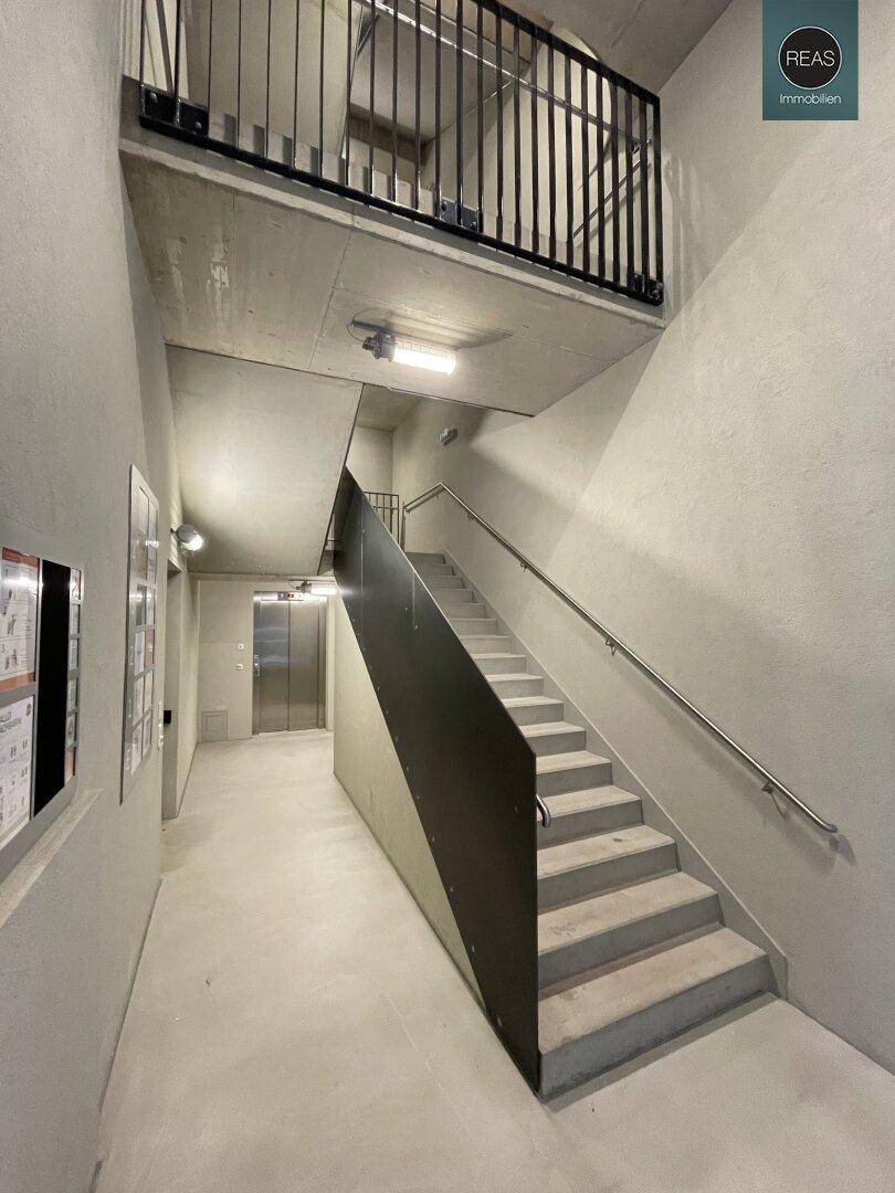 Modernes Treppenhaus mit Betonstufen, Metallgeländer und Zugang zum Aufzug in industriellem Stil.