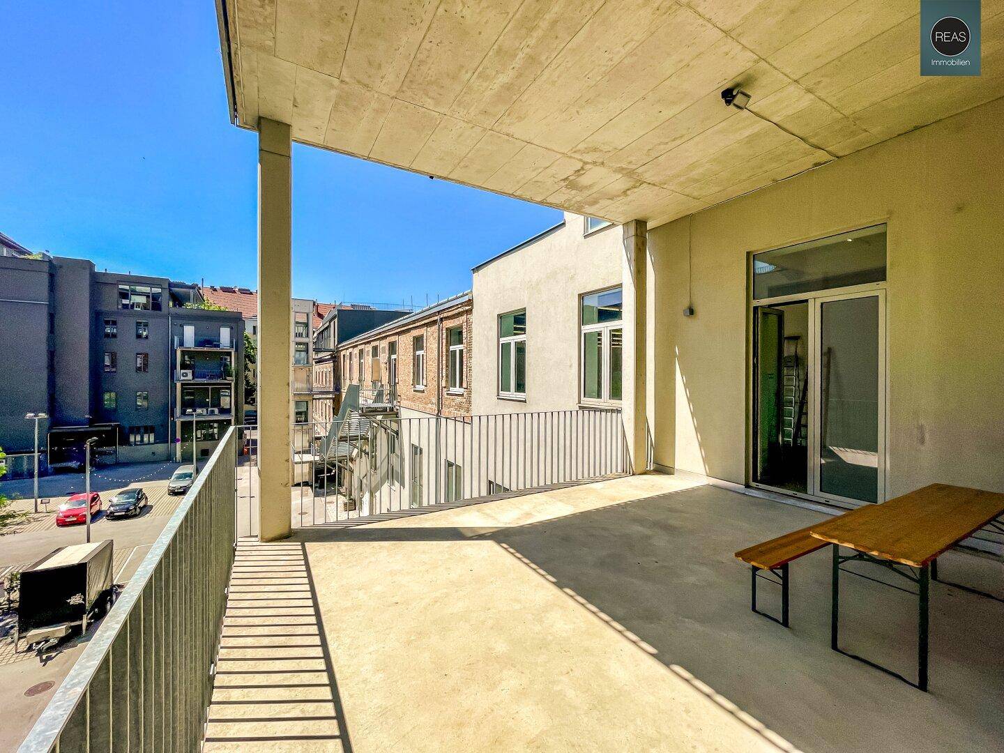 Großer Balkon mit Betonboden und Metallgeländer, bietet Blick auf die umliegenden Gebäude.