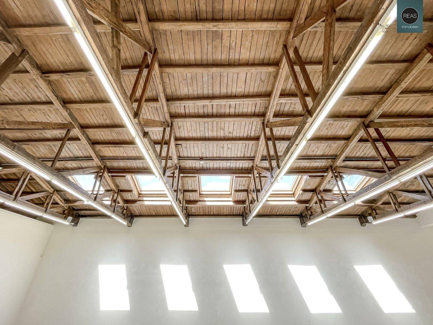 Blick auf die beeindruckende Holzbalkendecke mit integrierten Dachfenstern, die Licht spenden.