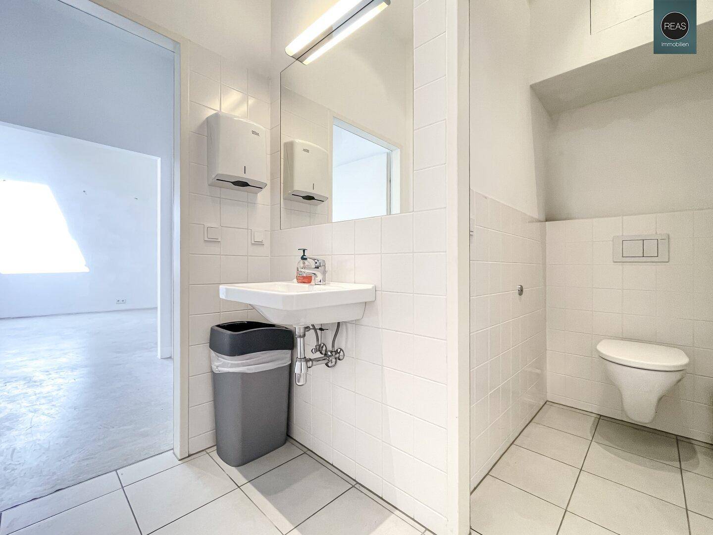 Helle Toilettenanlage mit weißen Fliesen, Waschbecken und wandhängendem WC.