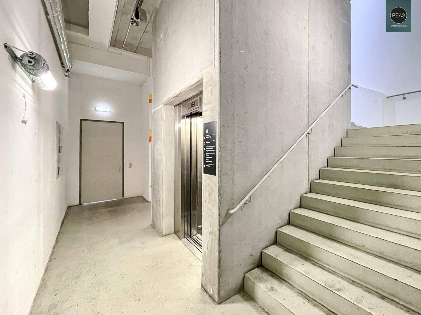 Treppenhaus und Aufzugsbereich mit Betonstufen und moderner Liftanlage.