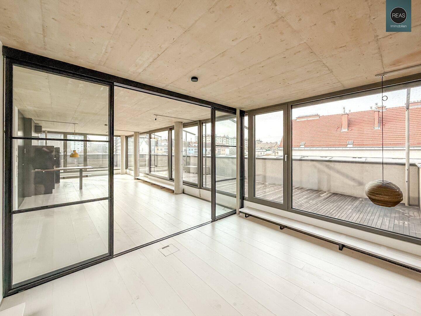 Heller, offener Raum mit Glaswänden, Holzboden und Blick auf die weitläufige Dachterrasse.