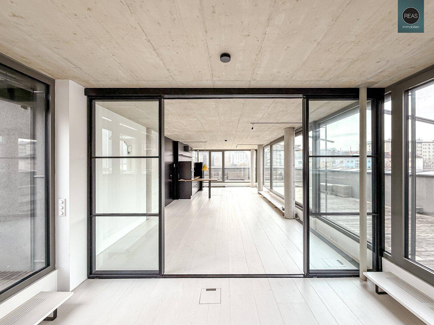 Heller, offener Raum mit Glaswänden, Holzboden und Blick auf die weitläufige Dachterrasse.