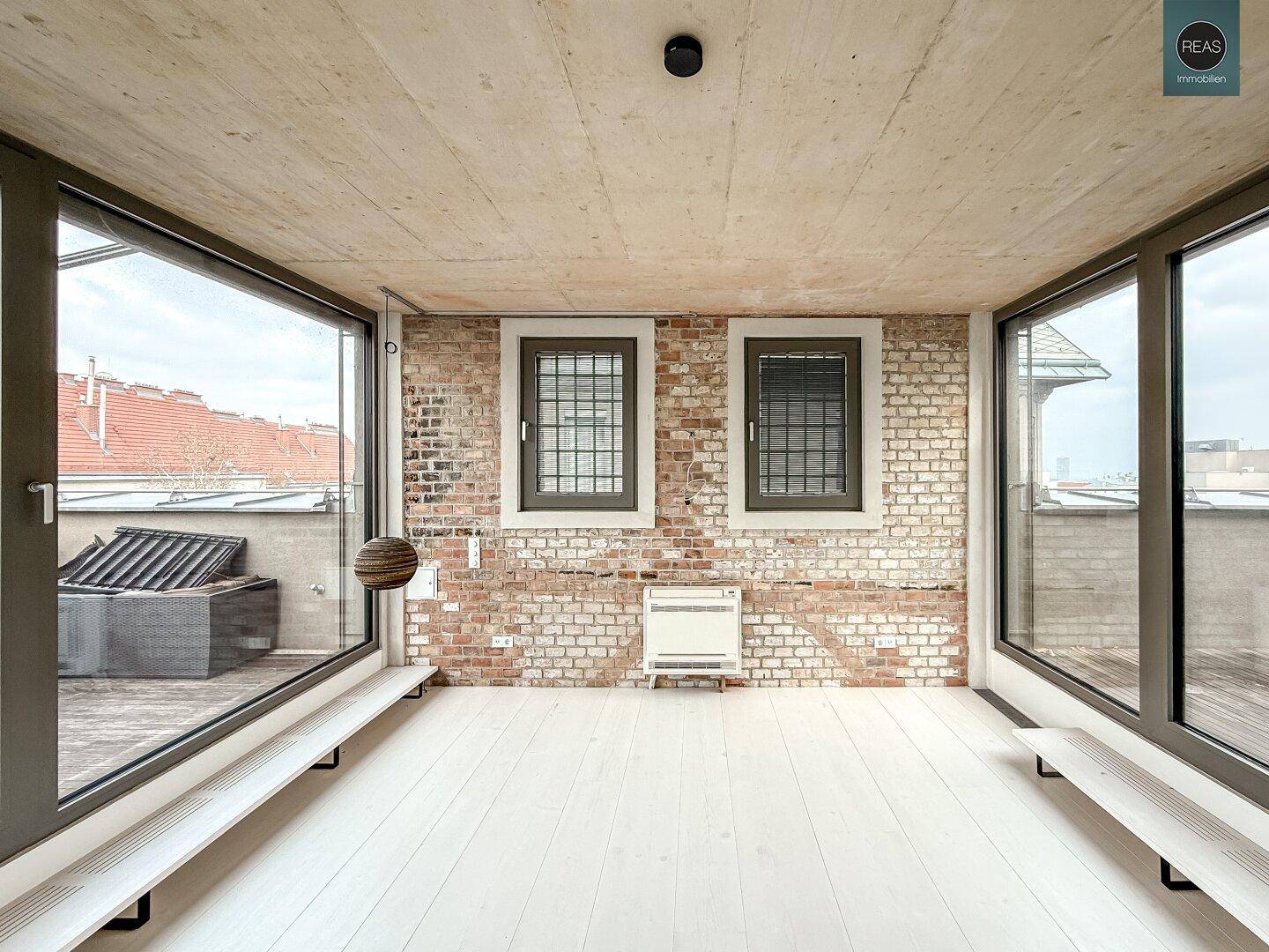 Leerer Konferenzraum mit Ziegelwand, großen Fenstern und Blick auf die weitläufige Dachterrasse.