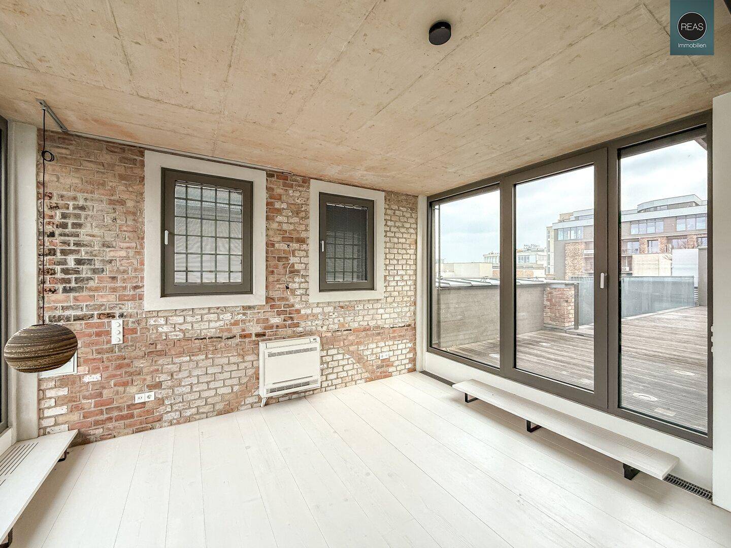 Leerer Konferenzraum mit Ziegelwand, großen Fenstern und direktem Zugang zur Dachterrasse.