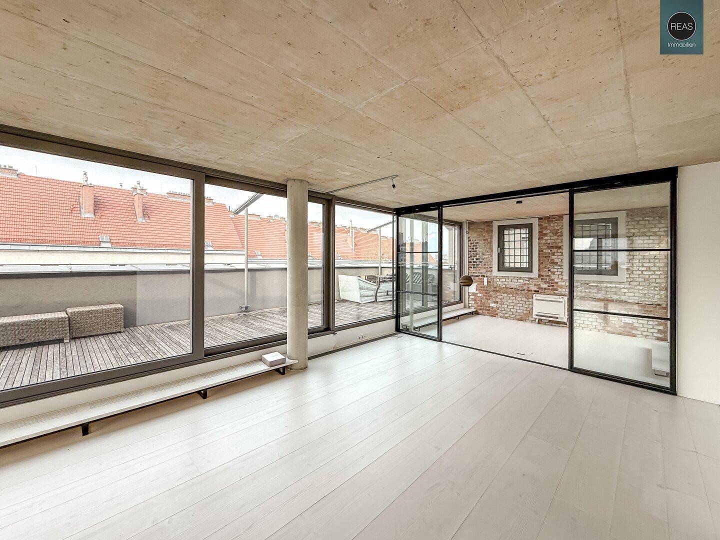 Heller, offener Raum mit weißem Holzboden und Blick auf die weitläufige Dachterrasse, die zum Entspannen einlädt.