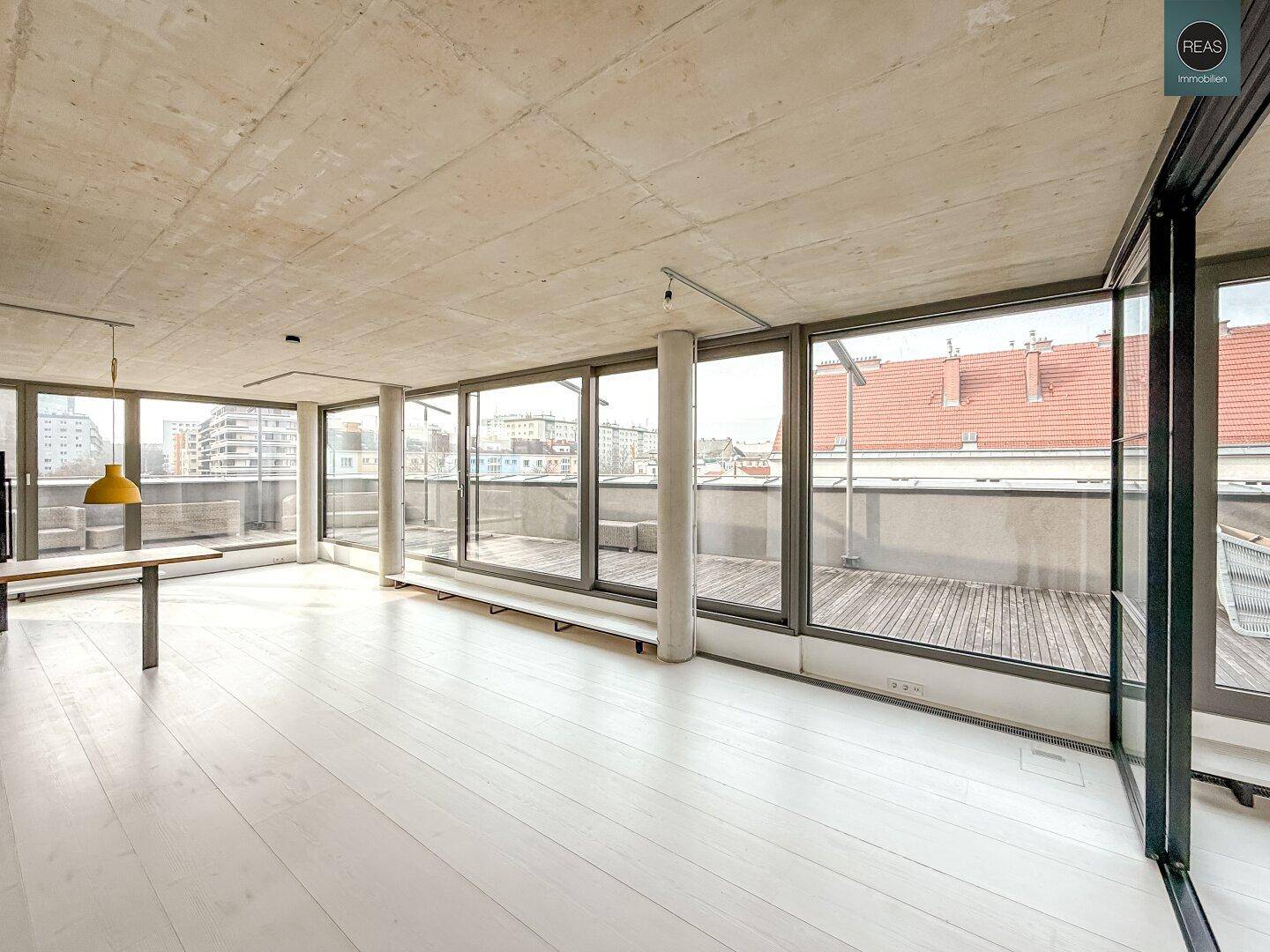Großer, heller Raum mit weißem Holzboden, Sichtbetondecke und Zugang zur weitläufigen Dachterrasse.