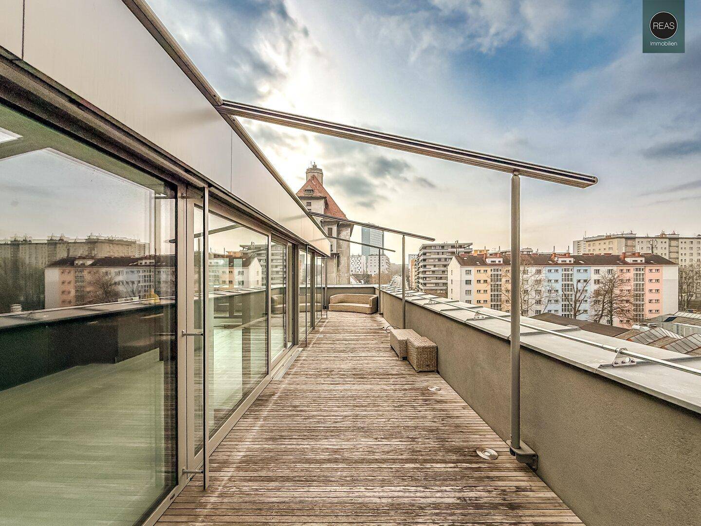 Weitläufige Dachterrasse mit Holzboden und Blick auf die umliegende Stadtlandschaft unter blauem Himmel.