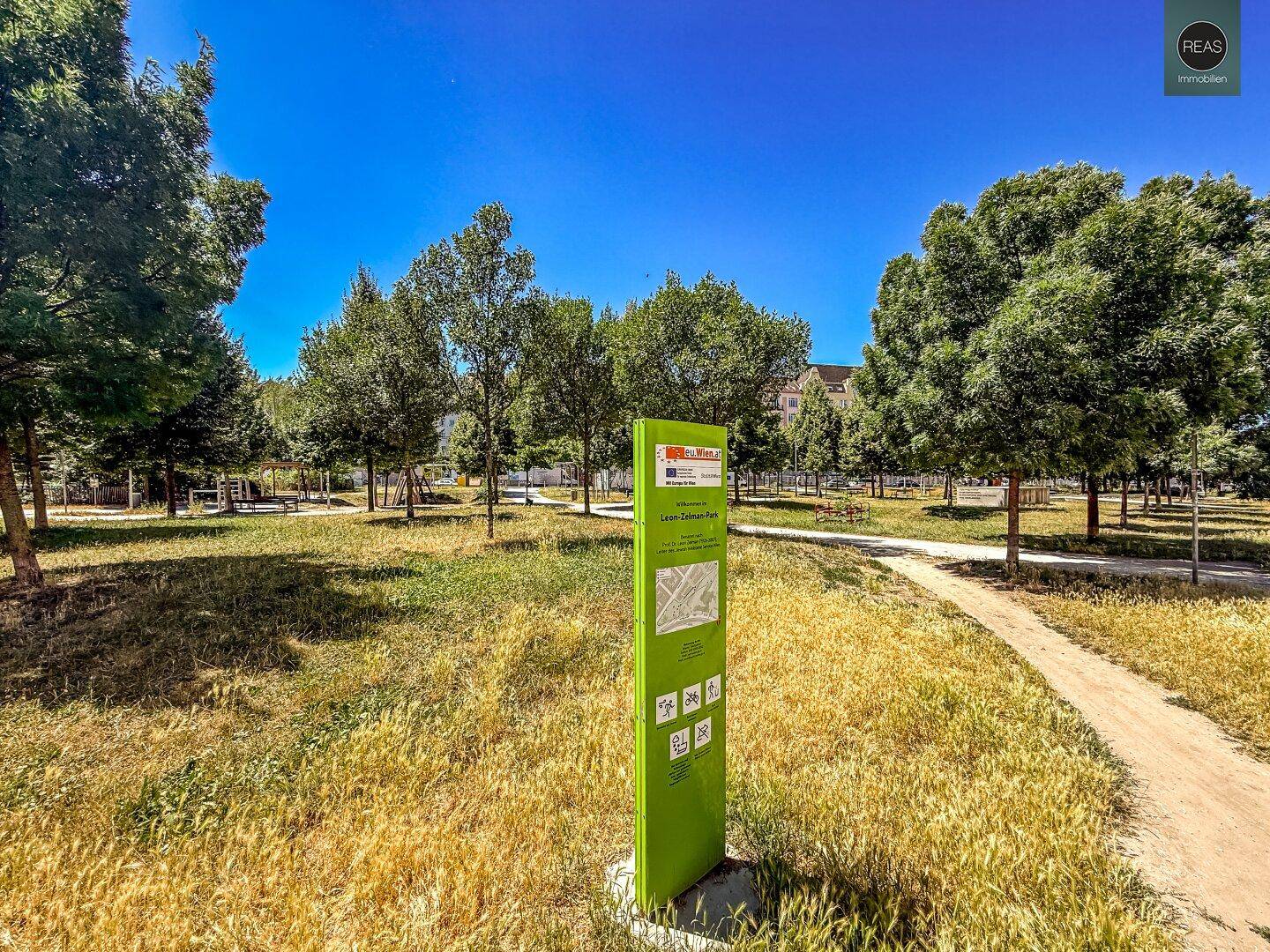 Großer, grüner Park mit Bäumen und einem Informationsschild, ideal zur Erholung.