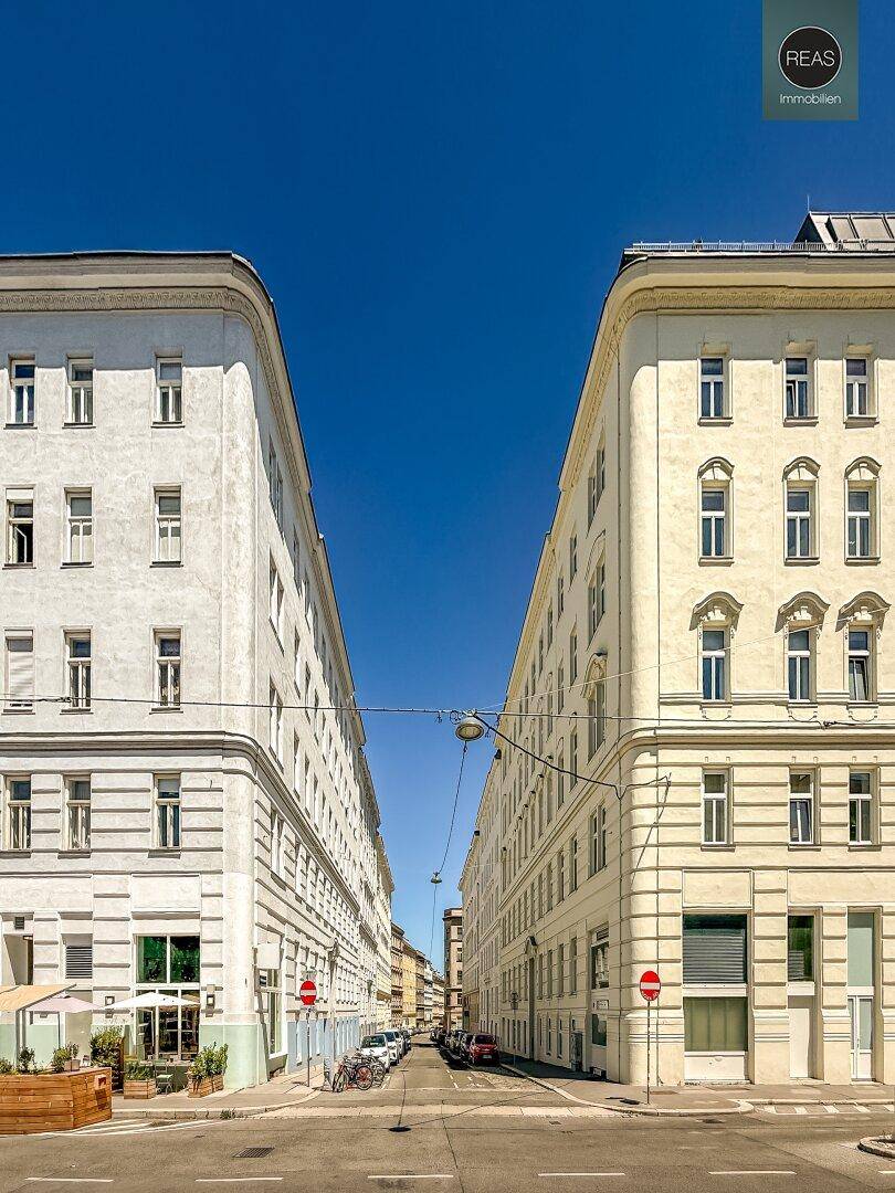 Weitläufige Stadtansicht mit zwei gegenüberliegenden Altbauten und einer Straße dazwischen.
