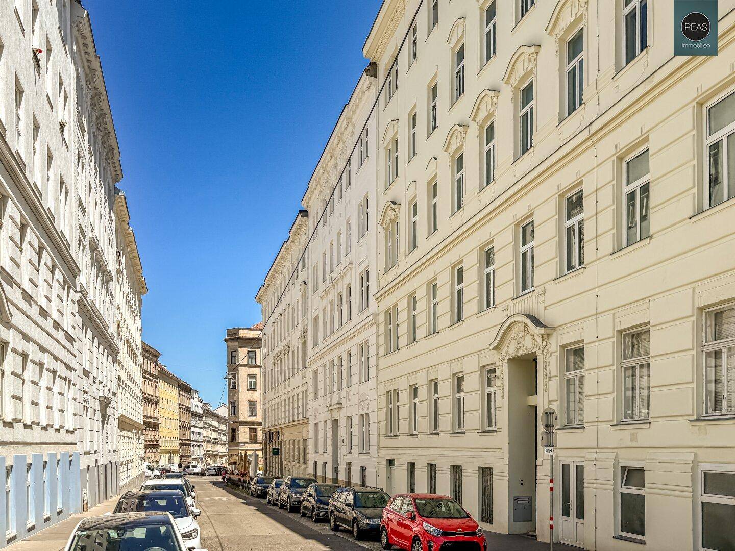 Historische Straßenzüge mit geparkten Autos und Altbauten unter blauem Himmel.