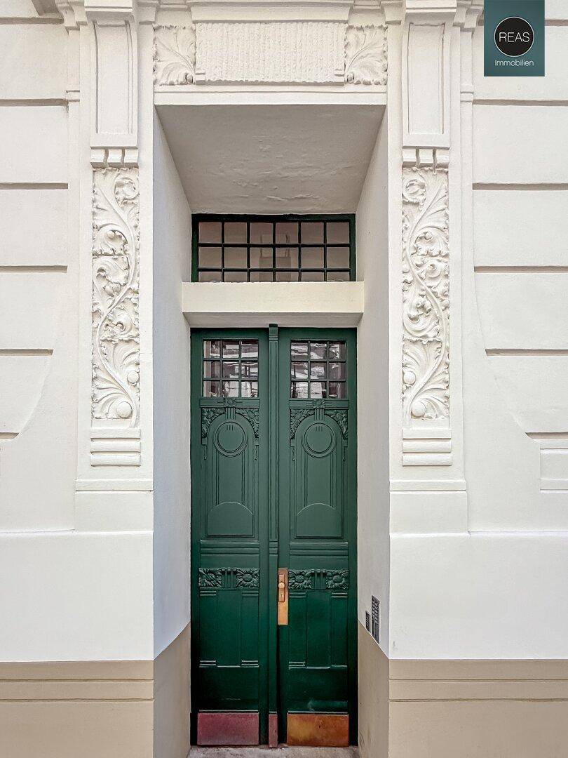 Detailansicht einer kunstvoll verzierten grünen Eingangstür in einer historischen Fassade.