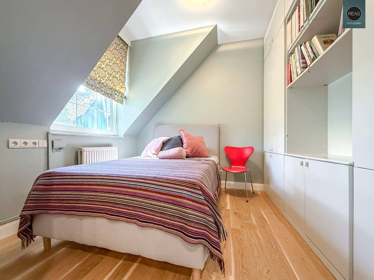 Gemütliches Schlafzimmer mit Einzelbett, Holzboden, schrägen Wänden und integrierten Bücherregalen.