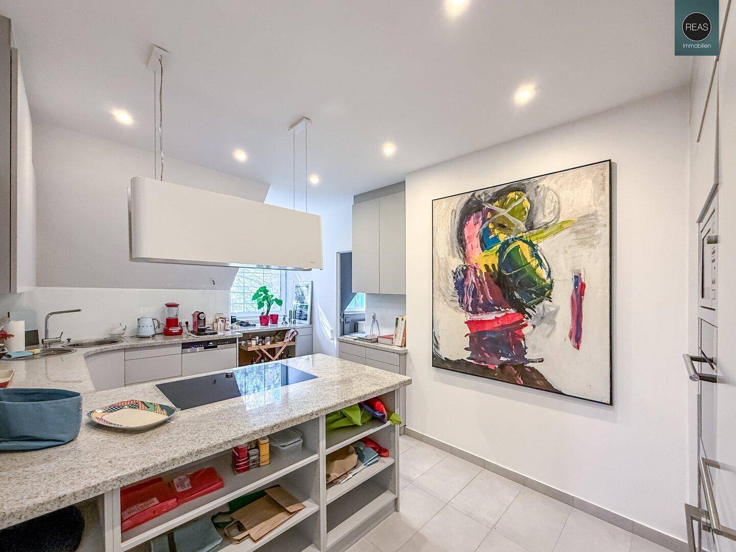 Helle Küche mit Kücheninsel, modernen Geräten und farbenfrohem Kunstwerk an der Wand.