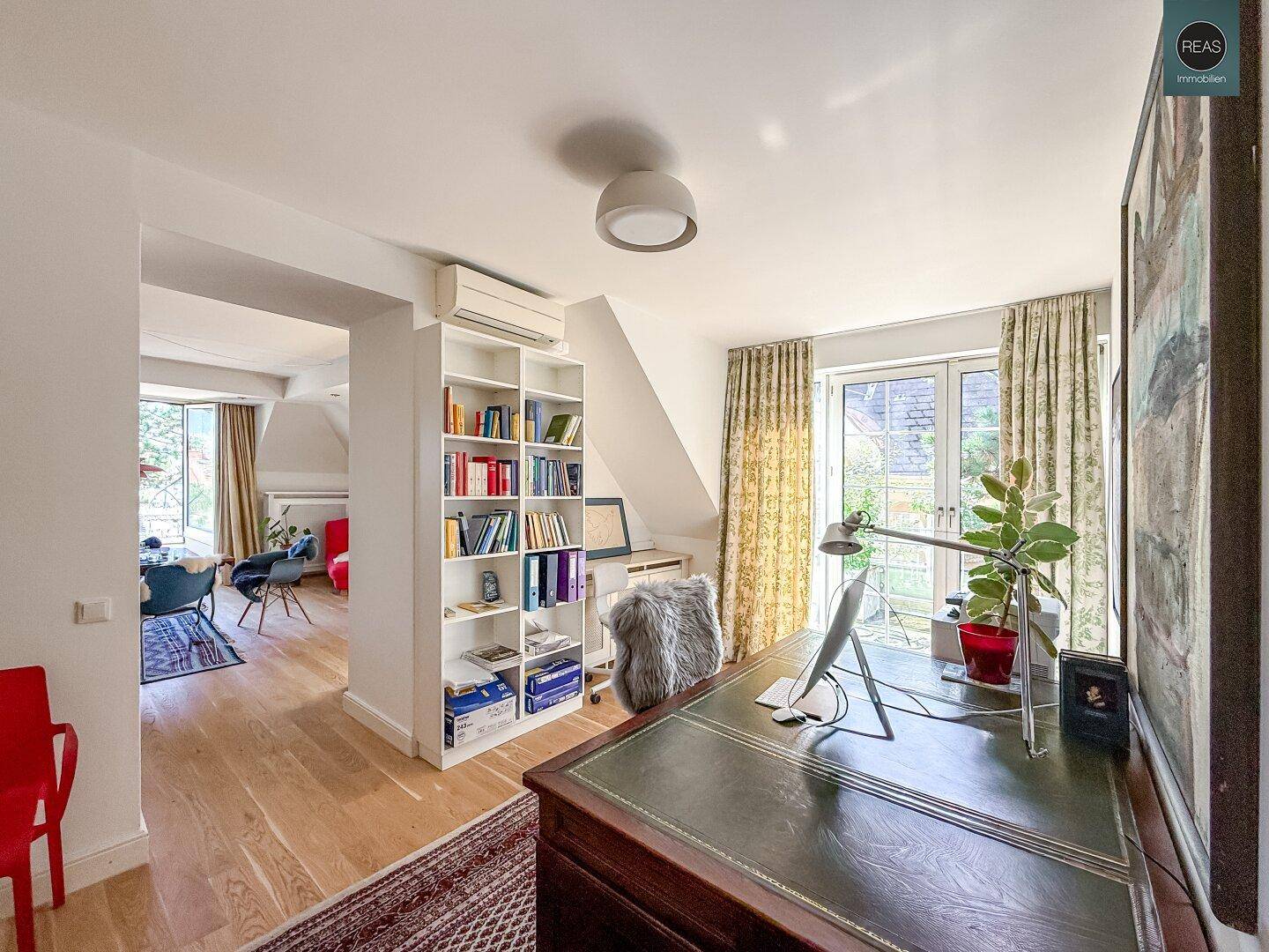 Helles Arbeitszimmer mit Holzboden, Bücherregal und Blick auf die grüne Terrasse.