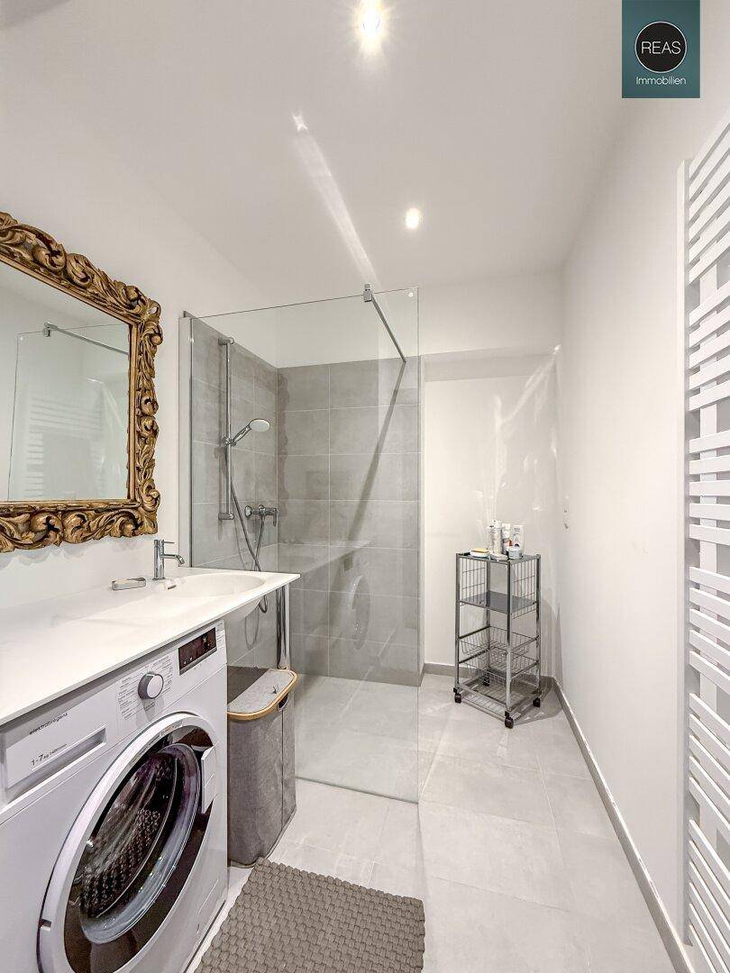 Modernes Badezimmer mit ebenerdiger Dusche, Waschmaschine und beheiztem Handtuchhalter.