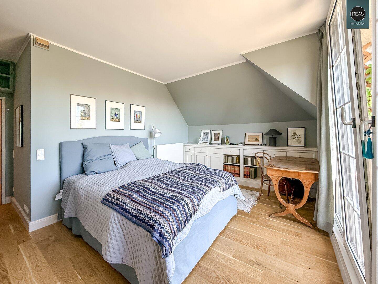 Helles Schlafzimmer mit Holzboden, Bett und Einbauschränken unter der Dachschräge.