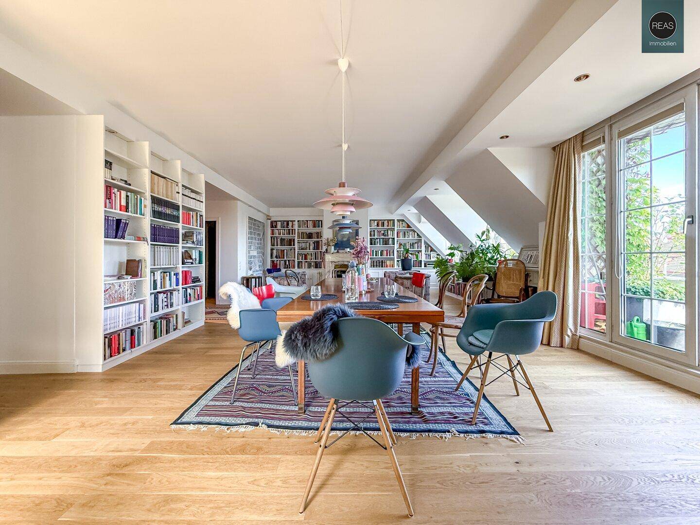 Heller Wohn- und Essbereich mit Holzboden, Bücherregalen und Zugang zu einer Außenterrasse.