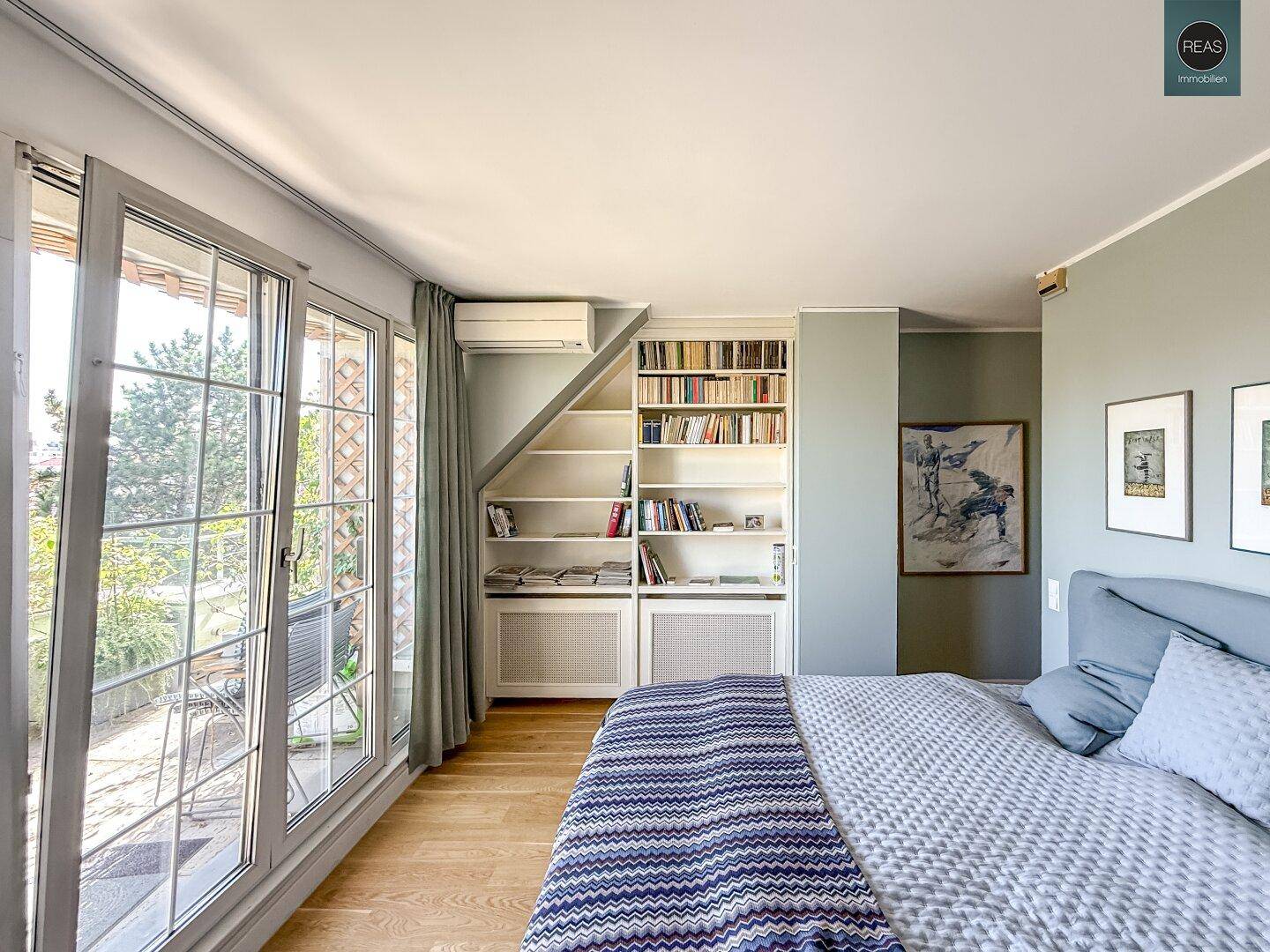 Helles Schlafzimmer mit Holzboden, Bett und Blick auf die grüne Terrasse.