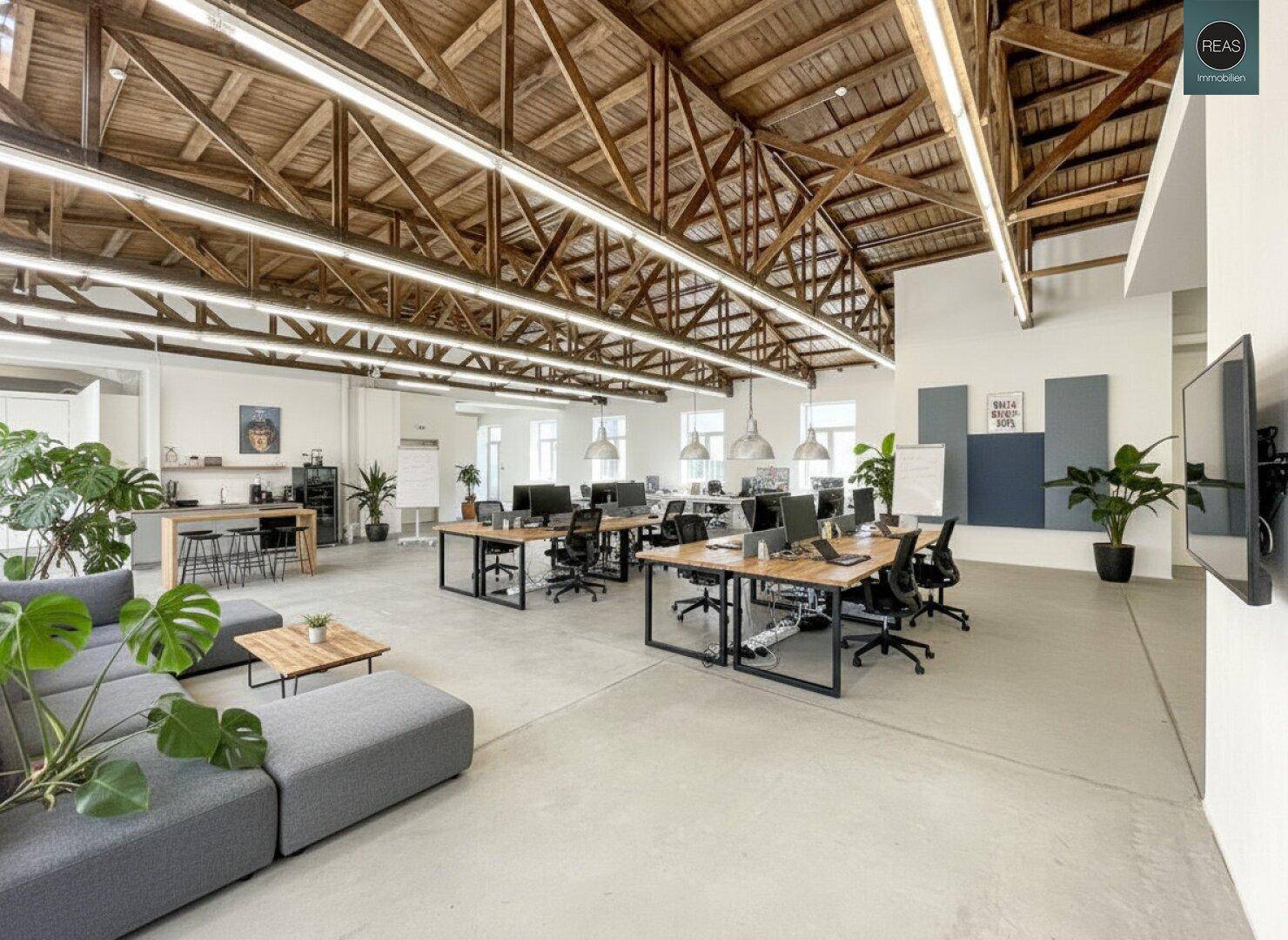 Moderner Bürobereich mit Schreibtischen, Lounge-Möbeln und einer integrierten Teeküche.