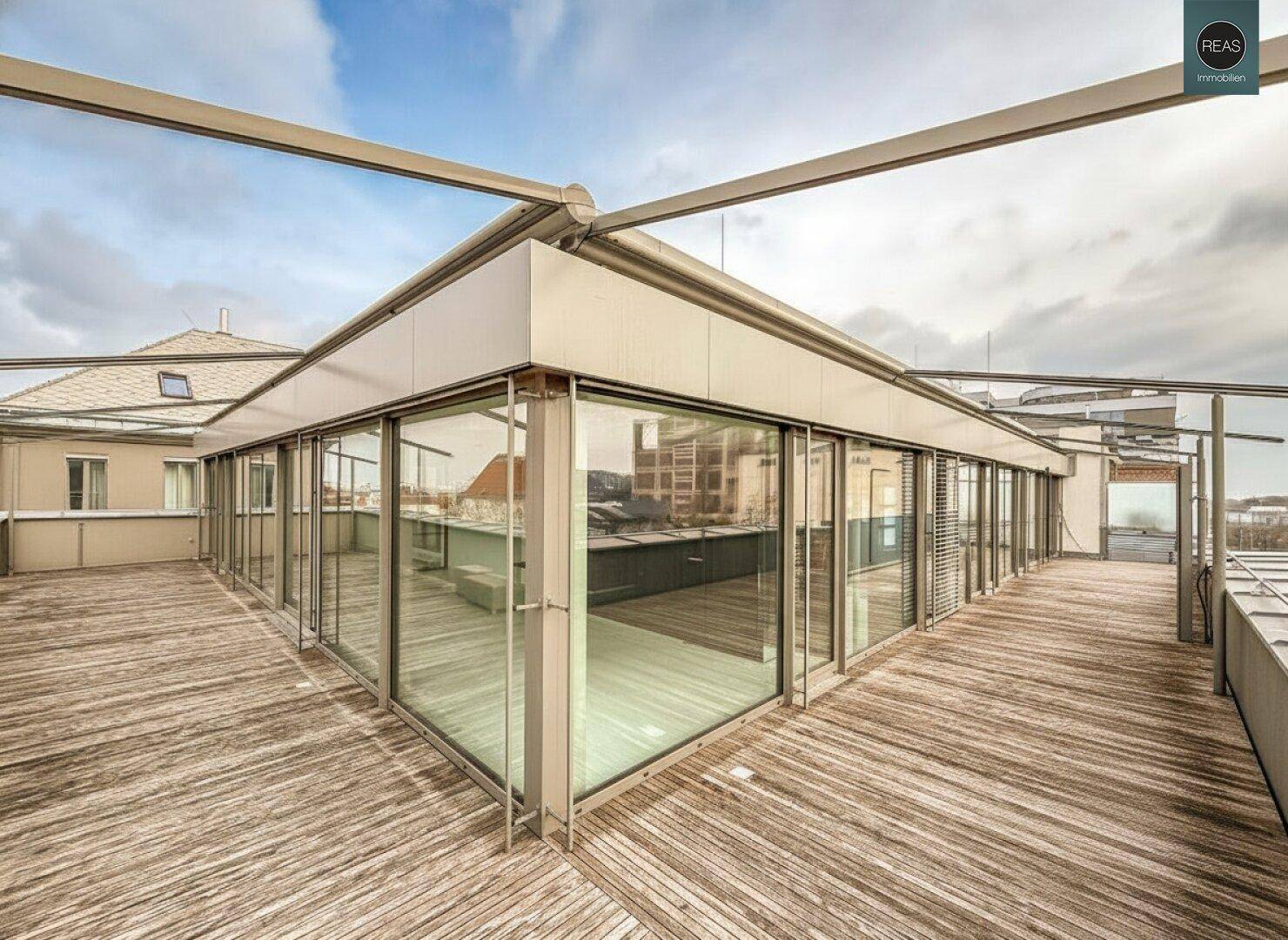 Weitläufige Dachterrasse mit Holzboden und Glasfassade, die den Innenbereich umschließt und Stadtblick bietet.