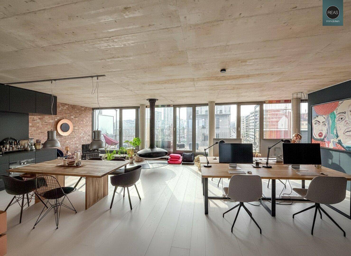 Geräumiger Loft-Bürobereich mit Holztisch, Schreibtischen und einem modernen Hängekamin in offener Gestaltung.