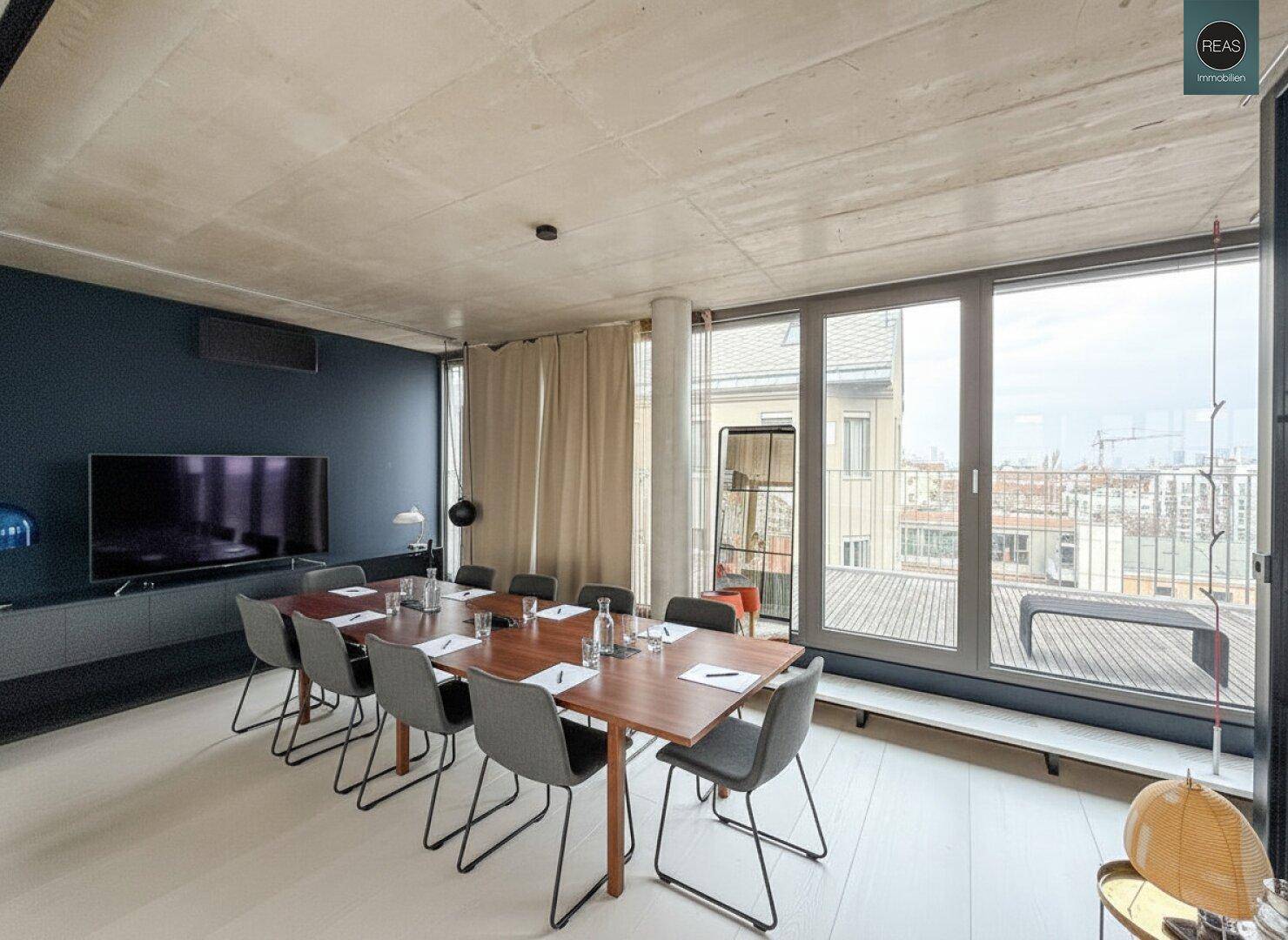 Konferenzraum mit großem Holztisch, bequemen Stühlen und weitem Stadtblick durch die raumhohen Fenster.