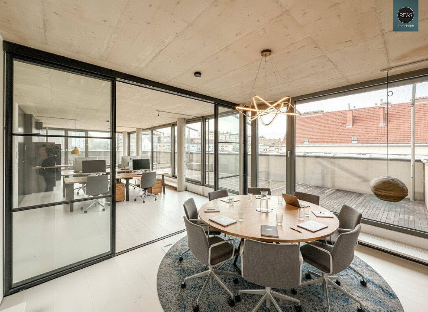Moderner Bürobereich mit Glaswänden, Schreibtischen und Blick auf die Dachterrasse, die zum Verweilen einlädt.
