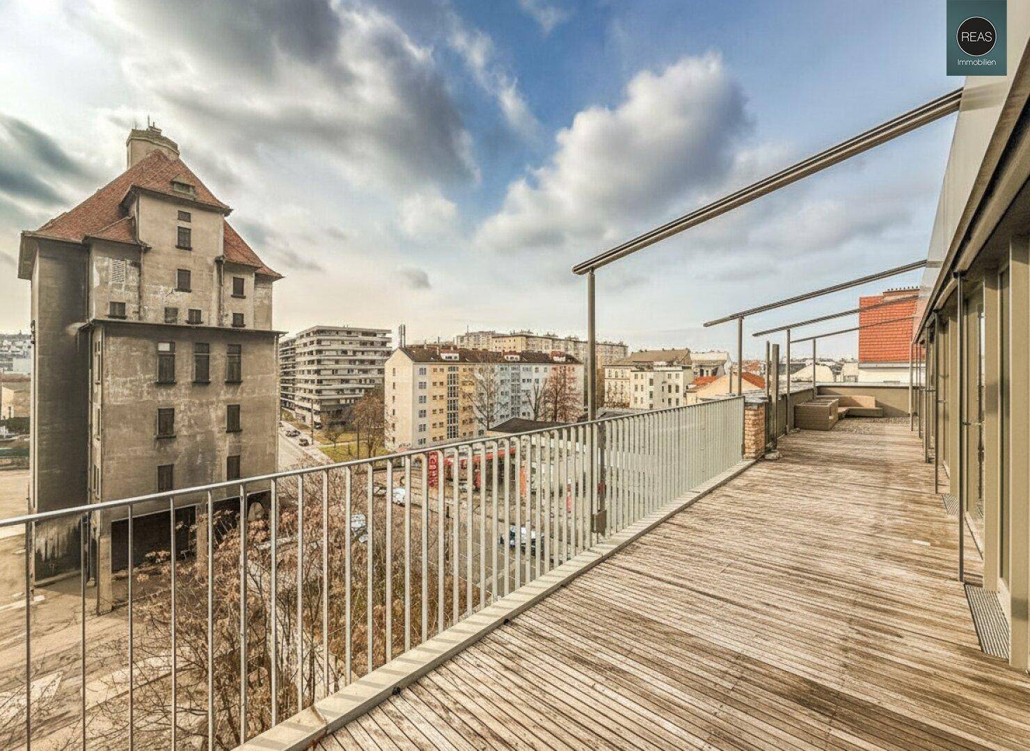 Weitläufige Dachterrasse mit Holzboden und Metallgeländer, die einen weiten Blick auf die Stadtarchitektur bietet.
