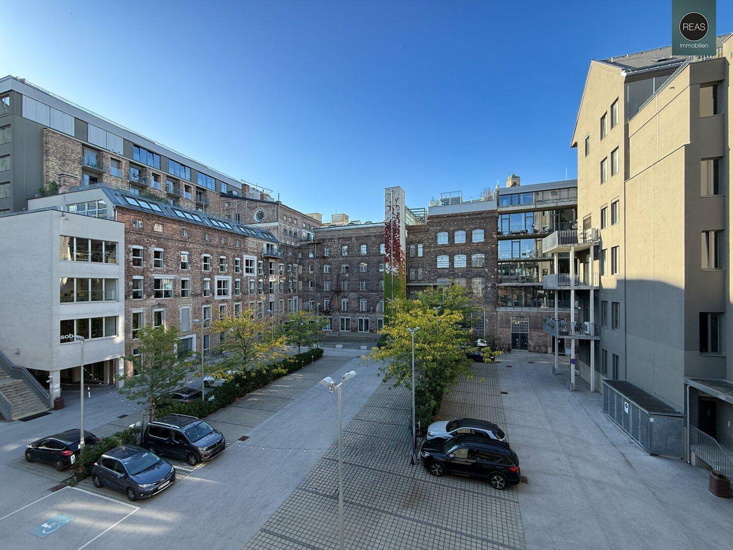 Weitläufiger Innenhof eines Gebäudekomplexes mit Parkplätzen und umliegenden historischen Gebäuden.