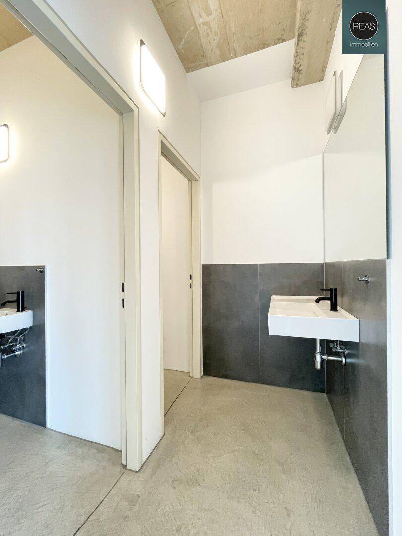Moderner Waschraum mit zwei Waschbecken, Spiegeln und schlichten weißen und grauen Fliesen.