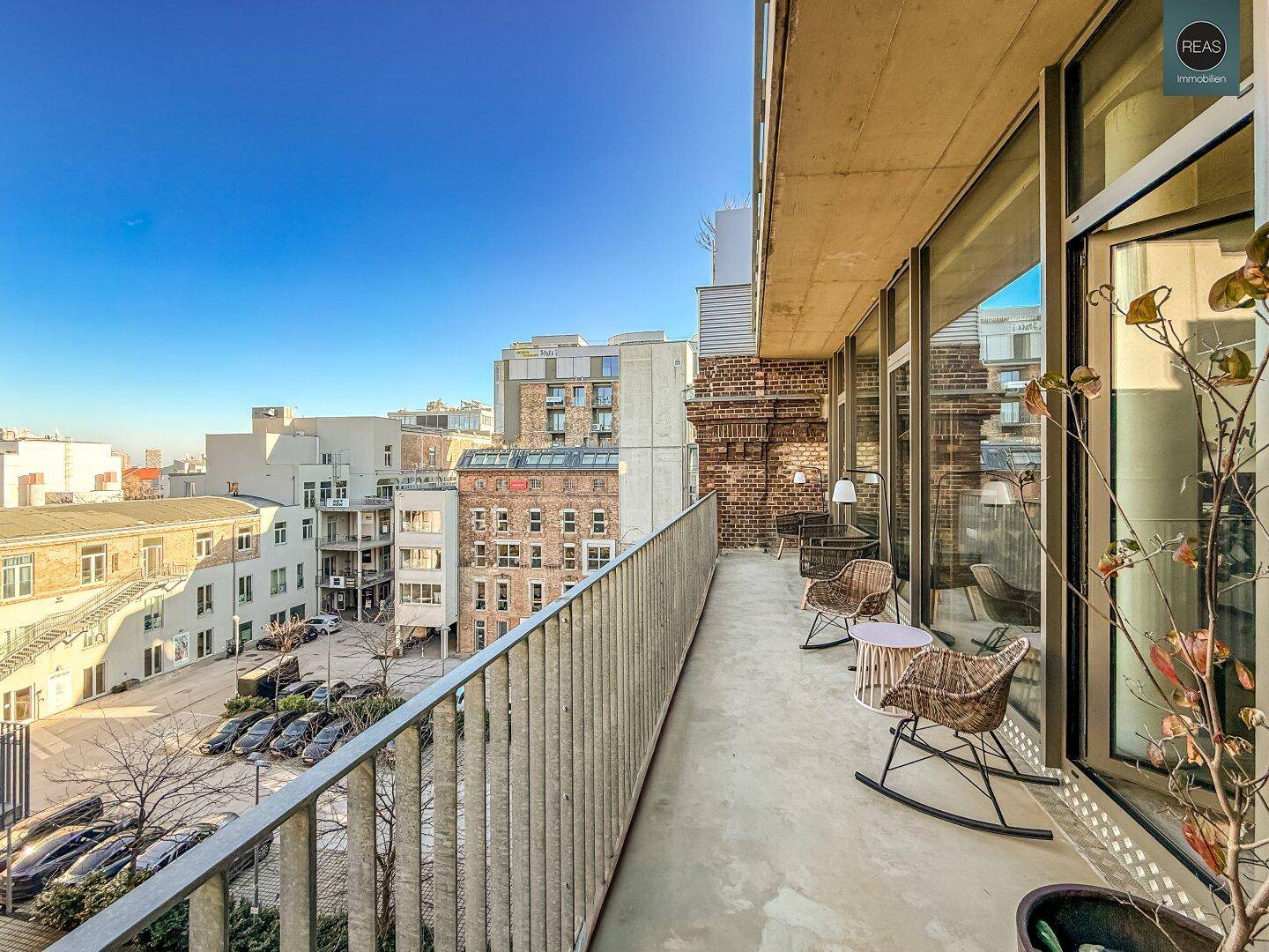 Langer Balkon mit Sitzgelegenheiten und Blick auf einen Innenhof und umliegende Gebäude.