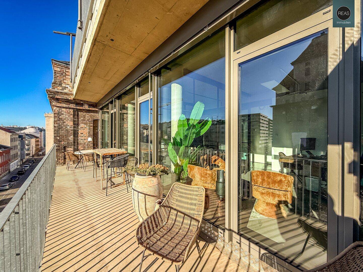 Sonniger Balkon mit Rattanmöbeln und Blick auf die Straße und die umliegenden Gebäude.