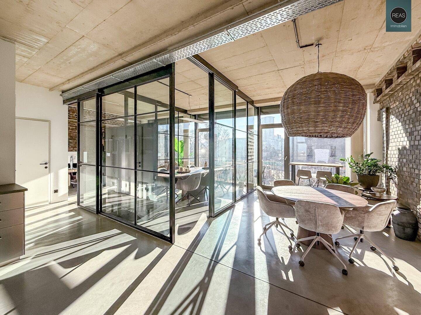 Moderner Bürobereich mit Glaswänden, Holztisch und Korbleuchte, der viel natürliches Licht erhält.