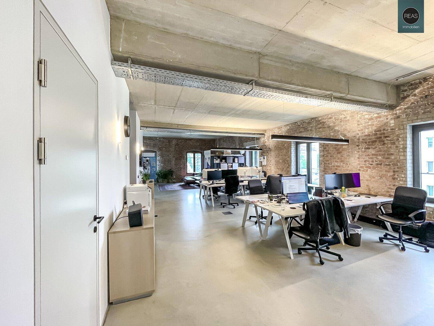 Moderner Büroraum mit Arbeitsplätzen, unverputzten Ziegelwänden und industriellem Charme.