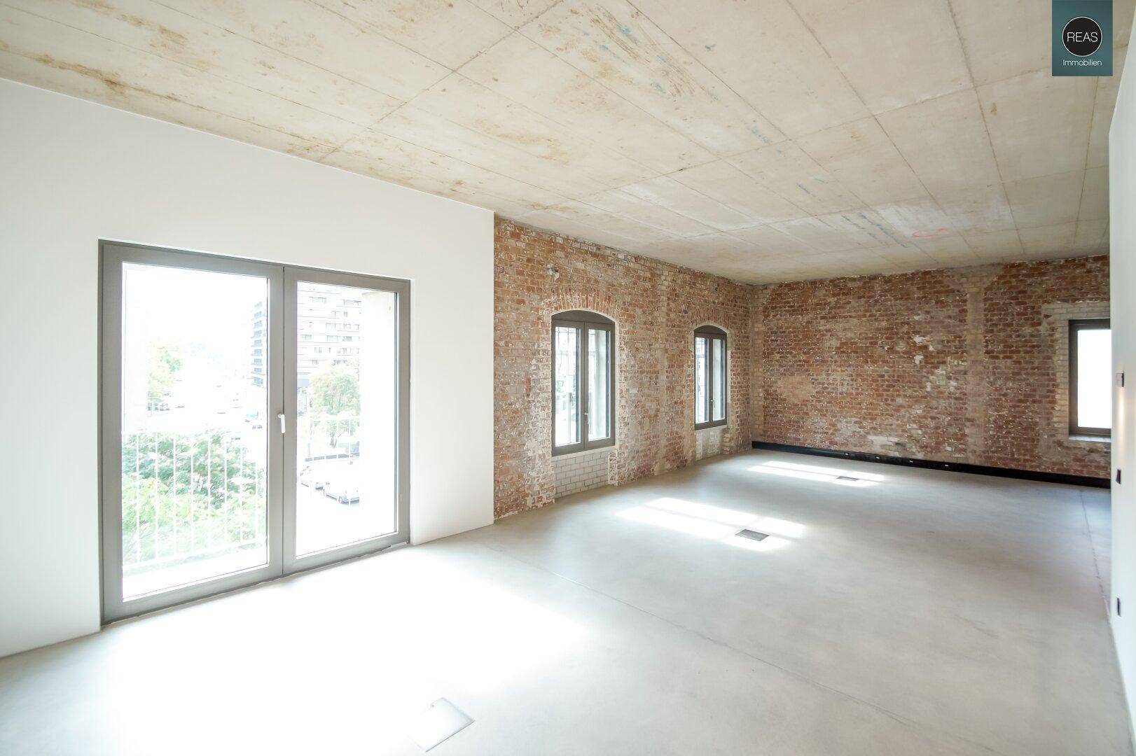 Geräumiger, heller Büroraum mit großen Fenstern und Zugang zu einem Balkon.