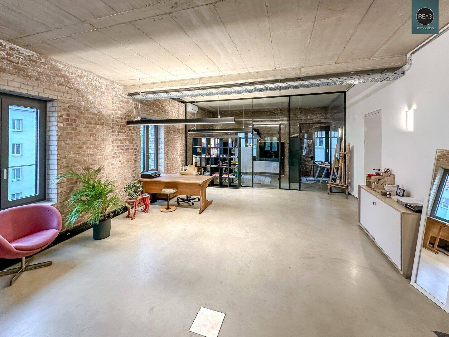 Moderner Büroraum mit Glaswänden, freiliegenden Ziegelwänden und industriellem Design.