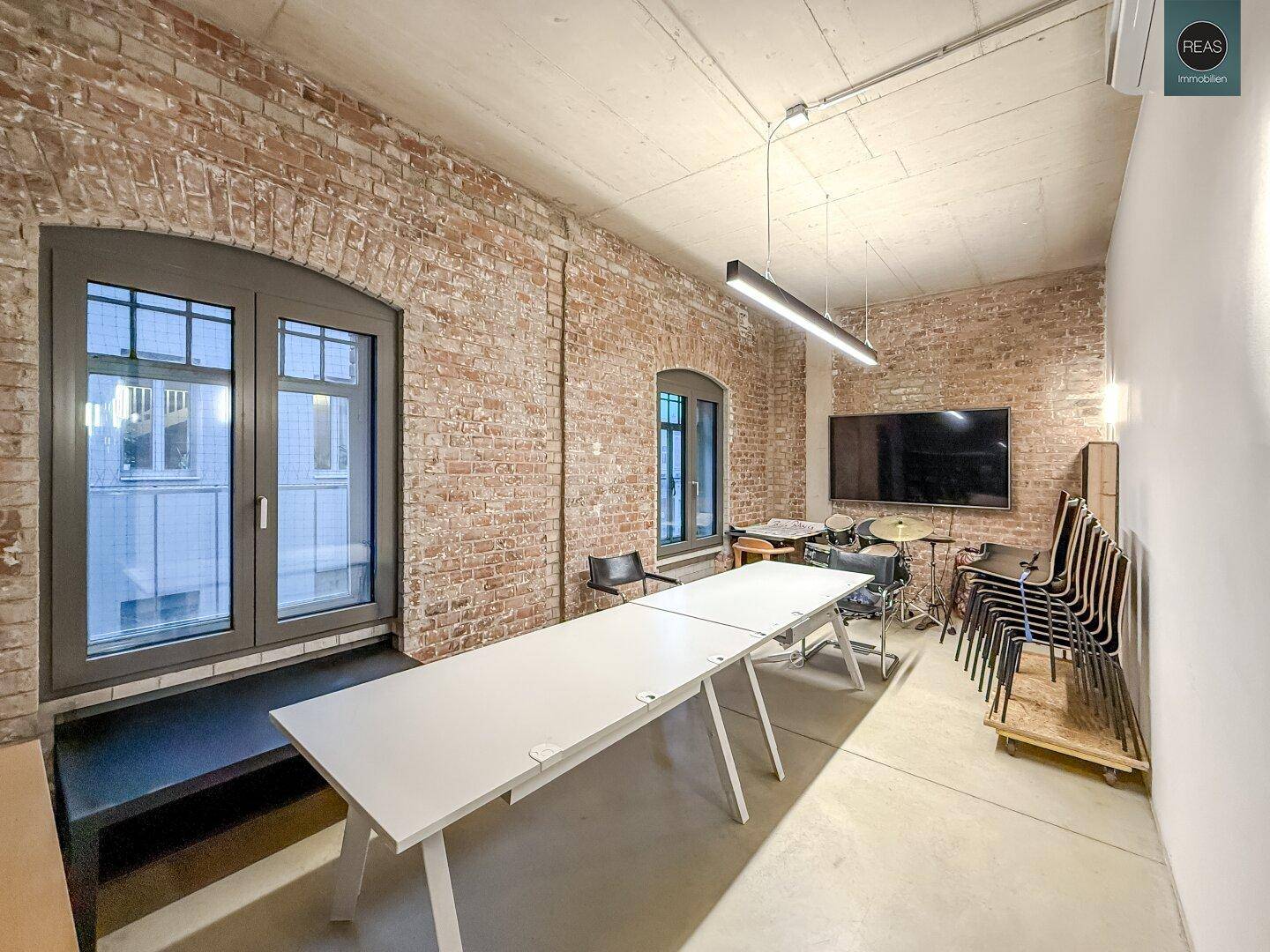 Großer Konferenzraum mit langem Tisch, Stühlen und einem großen Bildschirm an der Wand.