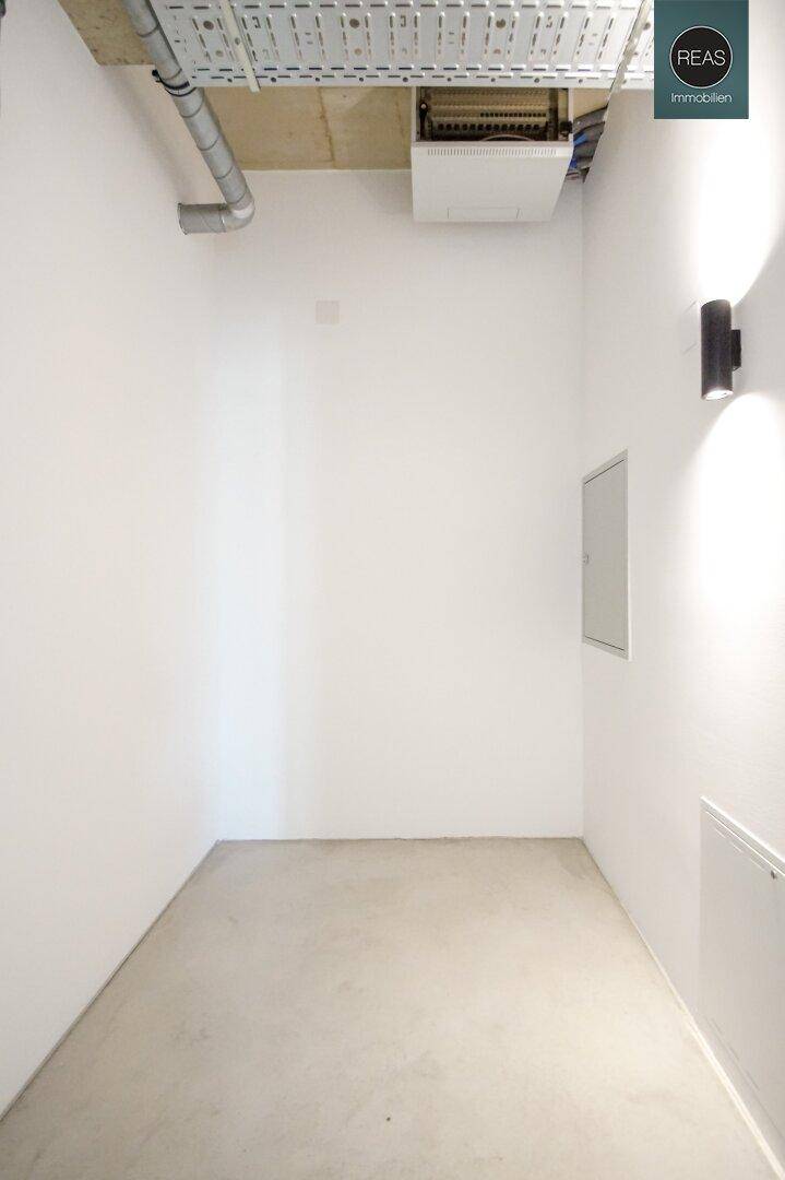 Kleiner, heller Raum mit weiß gestrichenen Wänden und sichtbaren Leitungen an der Decke.