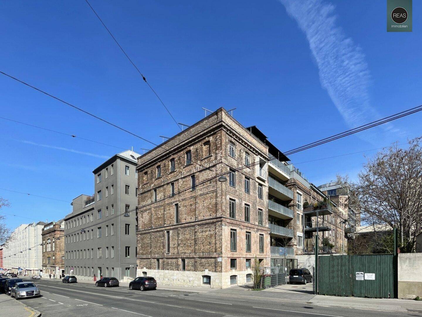 Historisches Backsteingebäude mit modernen Anbauten und Balkonen an einer städtischen Straße.