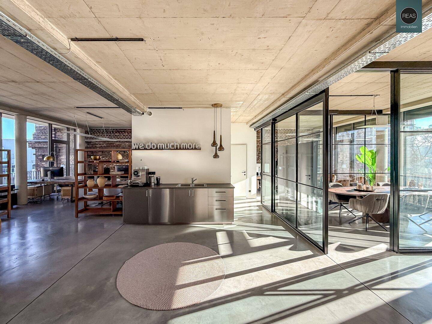 Moderner Bürobereich mit integrierter Küchenzeile, Glaswänden und viel Tageslicht, ideal für kreatives Arbeiten.
