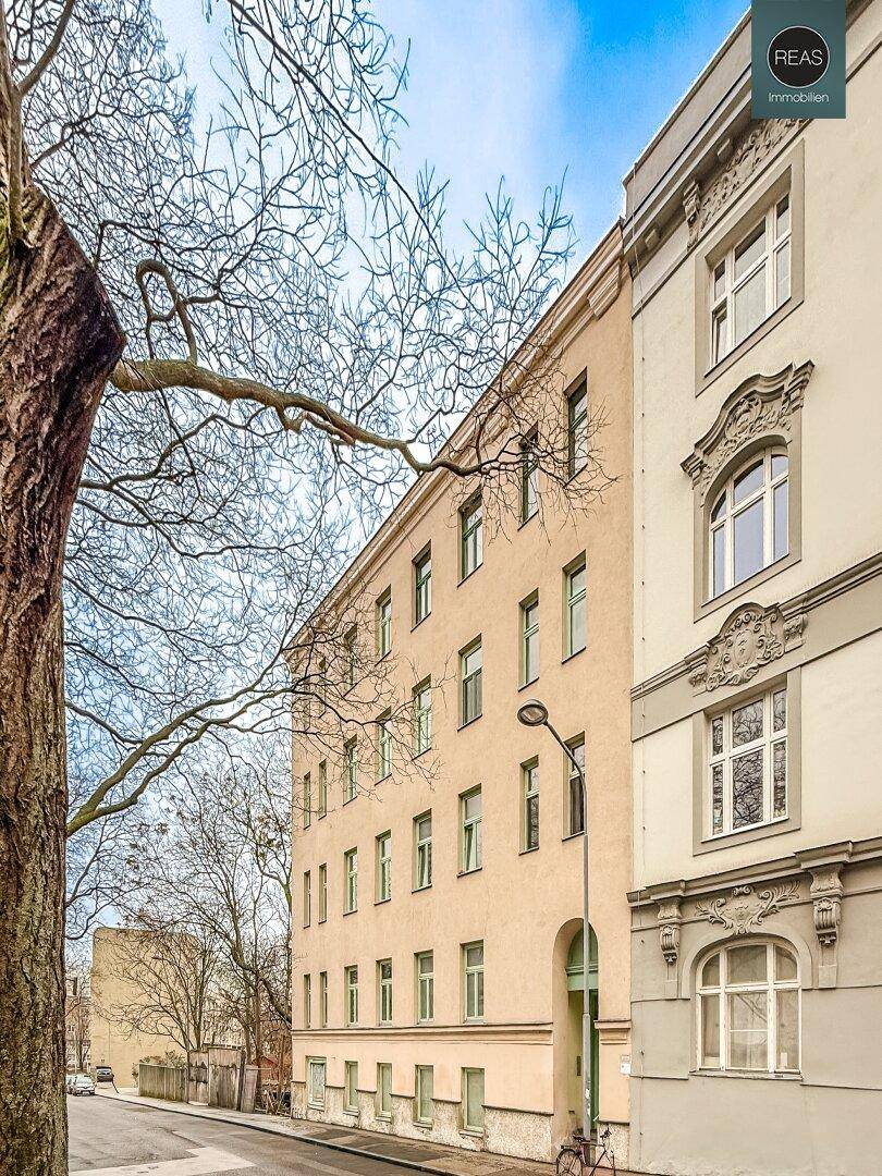Historisches Gebäude mit klassischer Fassade und vielen Fenstern, umgeben von Bäumen.