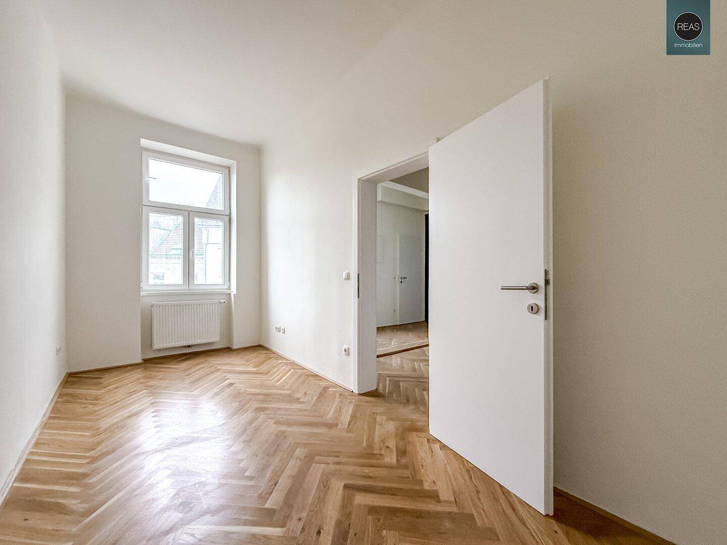 Leerer Raum mit Fischgrätparkett und einem Fenster, das viel Tageslicht hereinlässt, ideal für ein Büro.