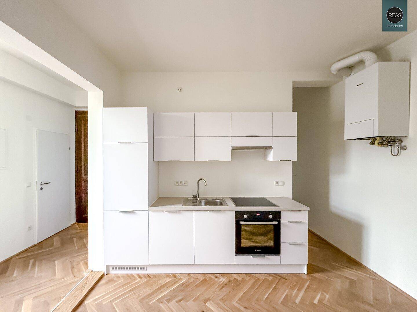 Voll ausgestattete, moderne weiße Küchenzeile mit Kühlschrank, Herd und Hängeschränken.
