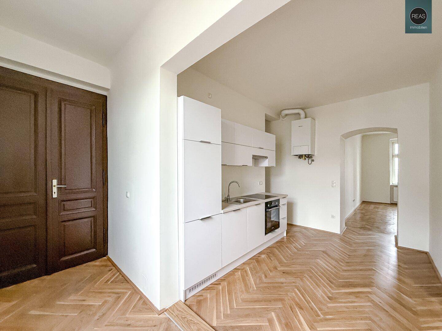 Kompakte, weiße Küchenzeile mit integriertem Kühlschrank und Herd, daneben eine traditionelle Holztür.