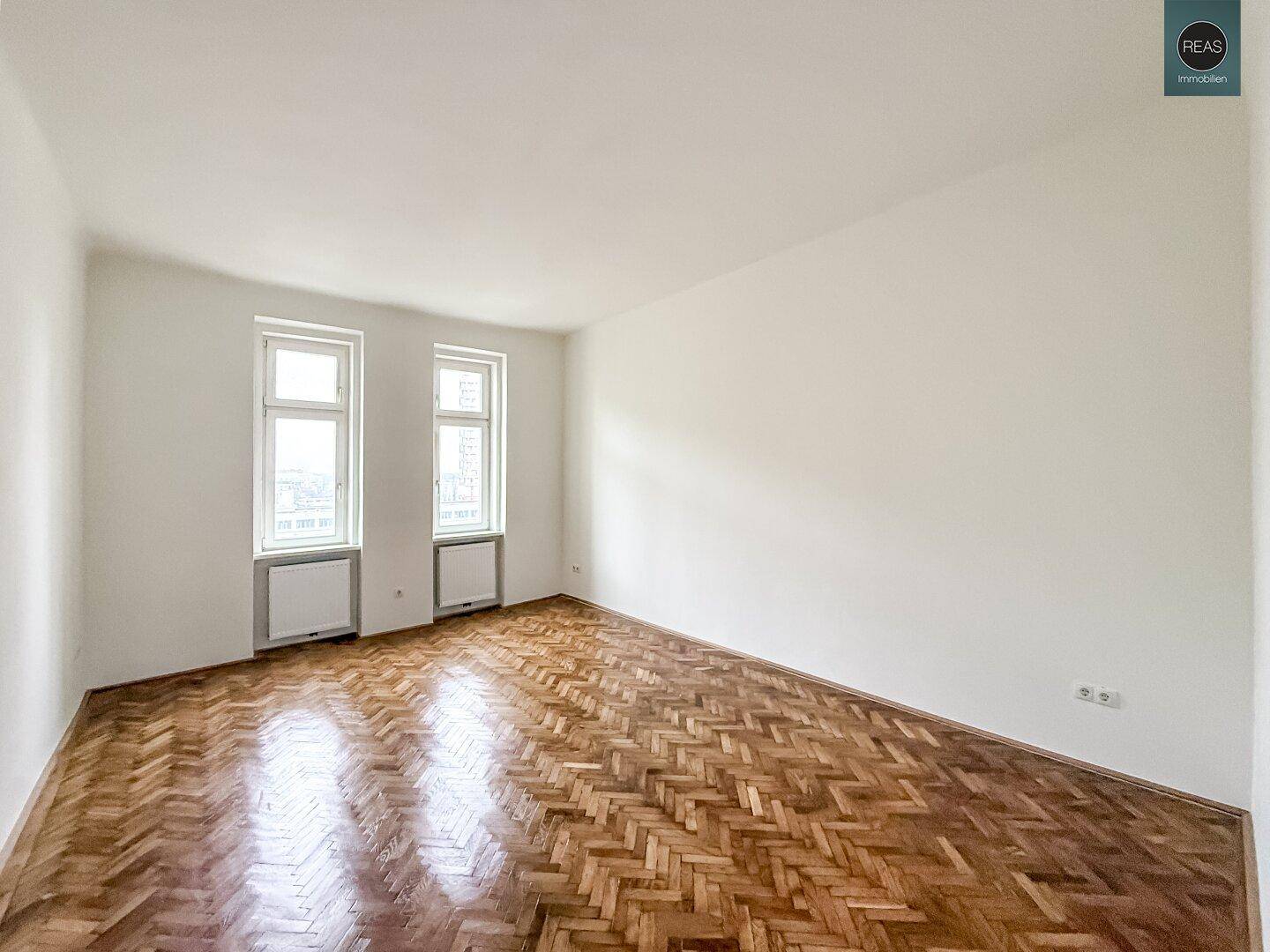 Heller, leerer Büroraum mit Fischgrätparkett und zwei großen Fenstern, ideal für flexible Nutzung.